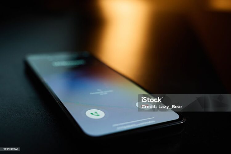 Close-up of smartphone lying on table in dark room with incoming call on screen. Concept of communication, technology, and mobile connection